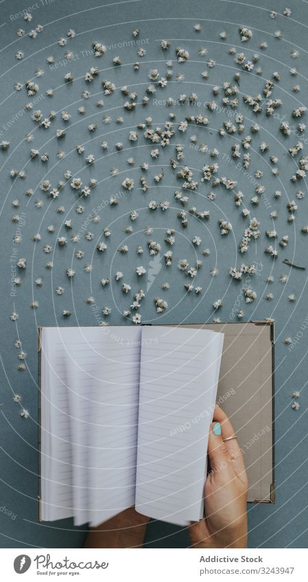 Person blättert leeres Notizbuch auf blauem Hintergrund mit winzigen Blumen Nachricht Notebook blanko Papier Streuung Hinweis Design Fliege Konzept Flip