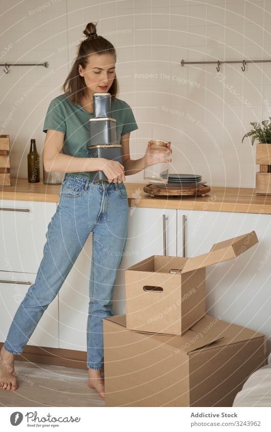 Vorsichtige Frau hält Behälter mit der Hand und nimmt Dosen aus dem Karton Appartement auspacken Küche Container Kasten bewegend Schachtel heimwärts Versand