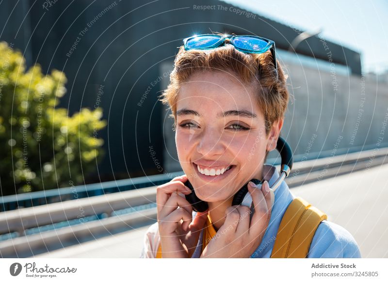 Verspielte trendige Frau auf der Straße bei Sonnenschein, die die Kamera mit den Händen bedeckt hell Lächeln spielerisch Sonnenbrille tausendjährig Kopfhörer