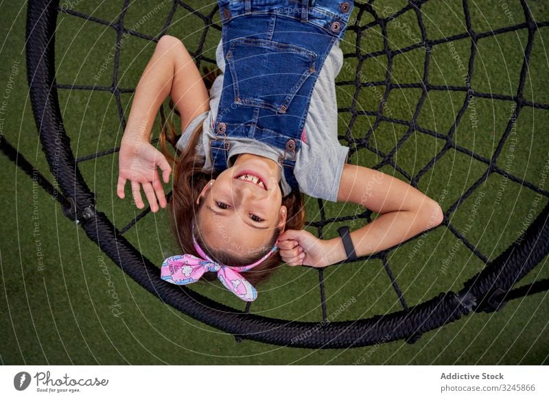 Glückliches Mädchen hat Spaß beim Korbschwingen pendeln spielen sorgenfrei Teenager Overall Spinnennetz Lügen Lächeln Spielplatz genießen aufgeregt spielerisch