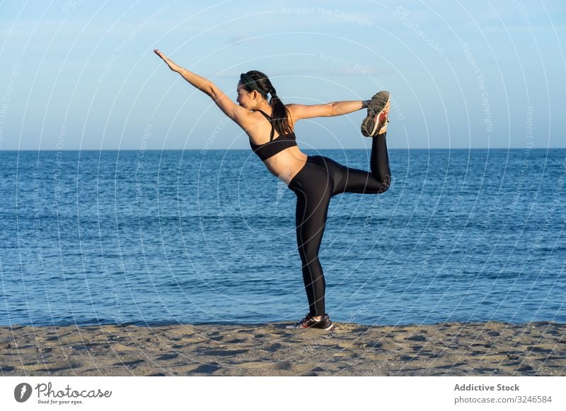 Zufriedene Sportlerin in aktiver Kleidung beim Yoga am Meeresufer Frau Körperhaltung Pose Einstellung Strand blau Himmel Training passen jung Sportbekleidung