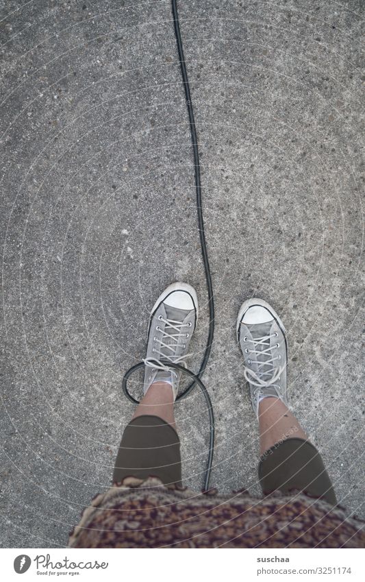 den fuß in der schlinge haben Füße Beine Frau stehen Kabel Schlaufe gefangen gefesselt Freiheitsberaubung laufen angekettet Straße Asphalt Vorsicht Gefahr