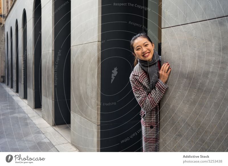 Fröhliche Asiatin ruht weiblich in legerer Kleidung und schaut aus moderner Gebäudewand an der Stadtstraße Frau Straße reisen Tourist Tür Peer schauen Sie