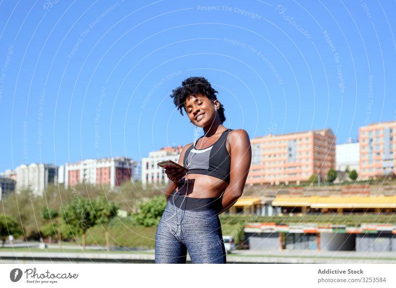 Fröhliche afroamerikanische Sportlerin hört Musik auf ihrem Smartphone Musik hören Großstadt Glück Lächeln Frau sportlich Kopfhörer Telefon Mobile Flussufer