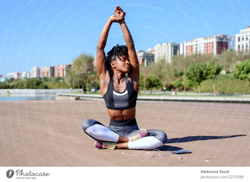 Afroamerikanische sportliche Frau, die in Lotus-Pose sitzt und die Hände nach oben streckt Lotussitz strecken Sportlerin Großstadt ruhen Erholung üben Yoga Zen