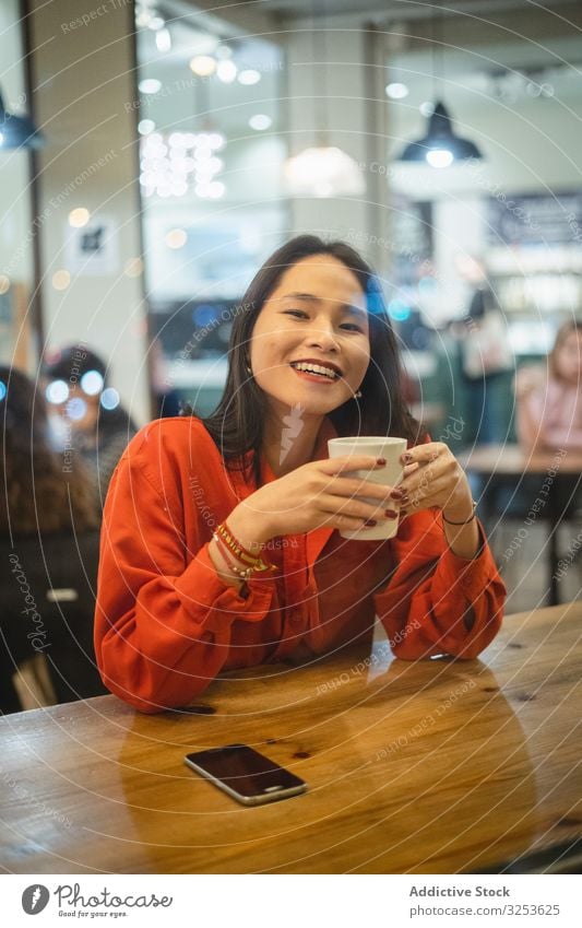 Frau bei einer Tasse Kaffee Café trinken Smartphone benutzend Lächeln modern Browsen Gerät Apparatur soziale Netzwerke Surfen zuschauend erfreut Glück heiter