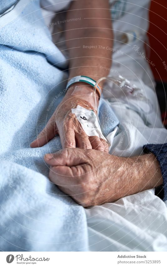 Älterer Mann hält Hand einer kranken Frau im Krankenhaus Paar älter Besucher geduldig Händchen haltend Kanüle Medizin Gesundheitswesen Bett Station Pflege