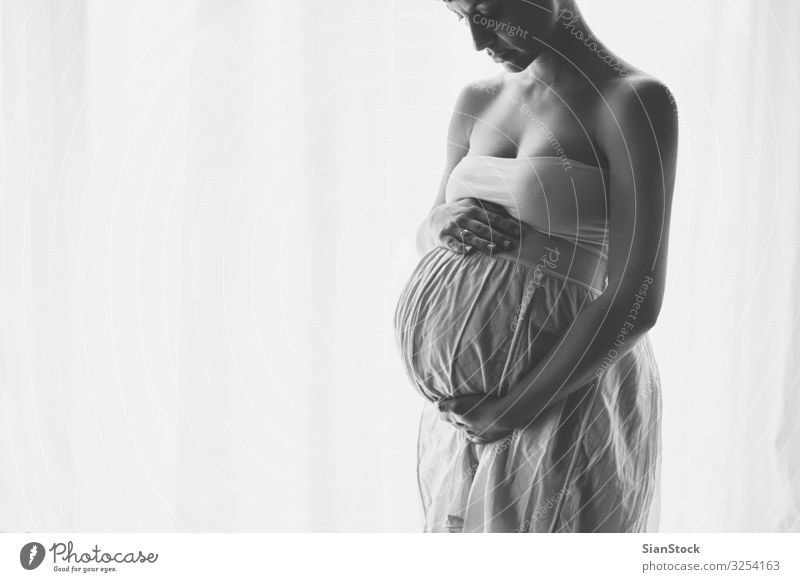 Junge schöne schwangere Frau steht zu Hause am Fenster Lifestyle Glück Körper Leben Mensch Baby Erwachsene Mutter Hand Kleid berühren Liebe sitzen schwarz weiß
