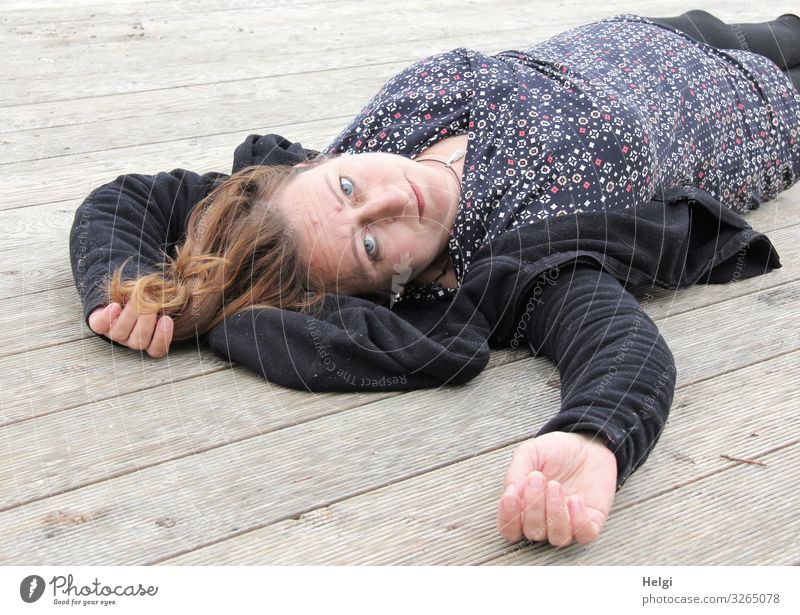 Frau mit langen brünetten Haaren und dunkler und gemusterter Kleidung liegt auf einem Holzboden Mensch feminin Erwachsene 1 45-60 Jahre Bekleidung Jacke