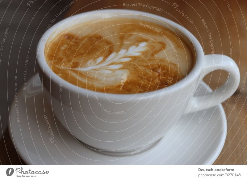 Weisse Kaffetasse auf weissem Untersetzer auf Holztisch. Kaffeeschaum mit Latte Art. Espresso Tasse Milch Schaum Kunst Barista Frühstück Innenaufnahme Koffein