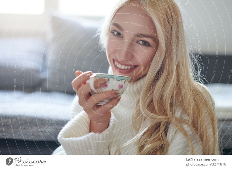 Hübsche Frau mit langen blonden Haaren trinkt Tee trinken Gesicht Winter Wohnung Sofa Wohnzimmer Erwachsene 1 Mensch 18-30 Jahre Jugendliche Lächeln niedlich