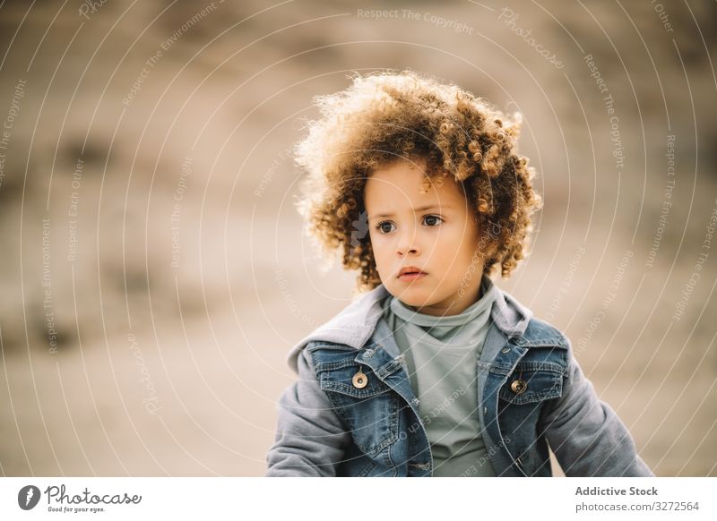 Ethnisches gelocktes Kleinkind über die Natur Kind Konzentration besinnlich bezaubernd lockig fokussiert Wind Mädchen lässig Menschliches Gesicht Porträt