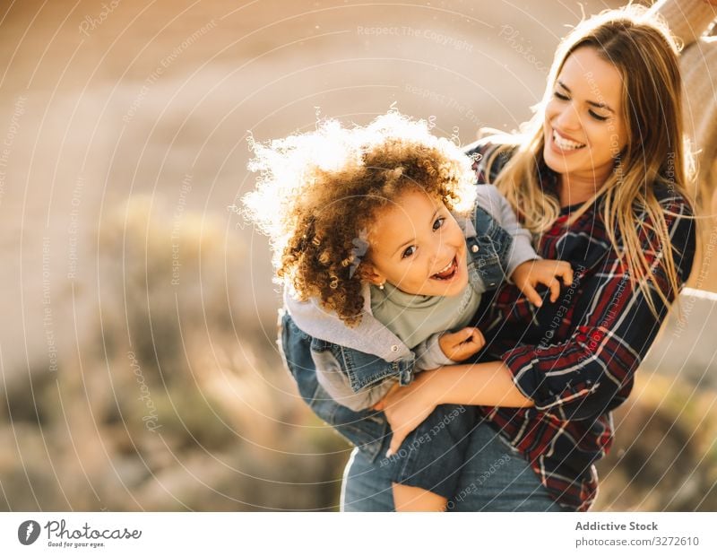 Fröhliche Frau spielt mit Kleinkind über die Natur Kind kuscheln Halt spielen Umarmen Lächeln Glück Kribbeln heiter Ausdruck krause Haare schwelgen Mutter Spaß