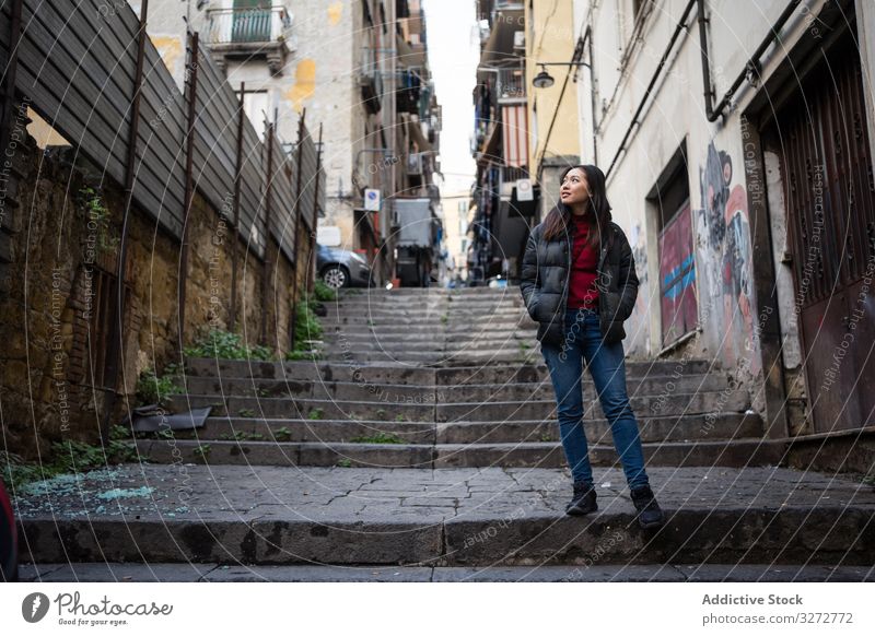 Ethnische Frau steht auf Stufen in schäbiger Straße Gebäude Schritt ethnisch Außenseite Großstadt Hände in den Taschen Lifestyle ruhen sich[Akk] entspannen cool
