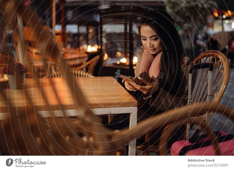 Asiatischer Reisender benutzt Smartphone im Cafe Frau Café benutzend Tourist Koffer ethnisch Abend Großstadt urban asiatisch Browsen soziale Netzwerke lässig