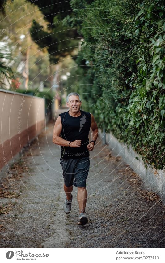 Alter Mann in guter Verfassung rennt auf Straße entlang Pflanzenzaun sportlich Joggen älter reif alt Form Training Läufer Athlet Fitness Großstadt passen