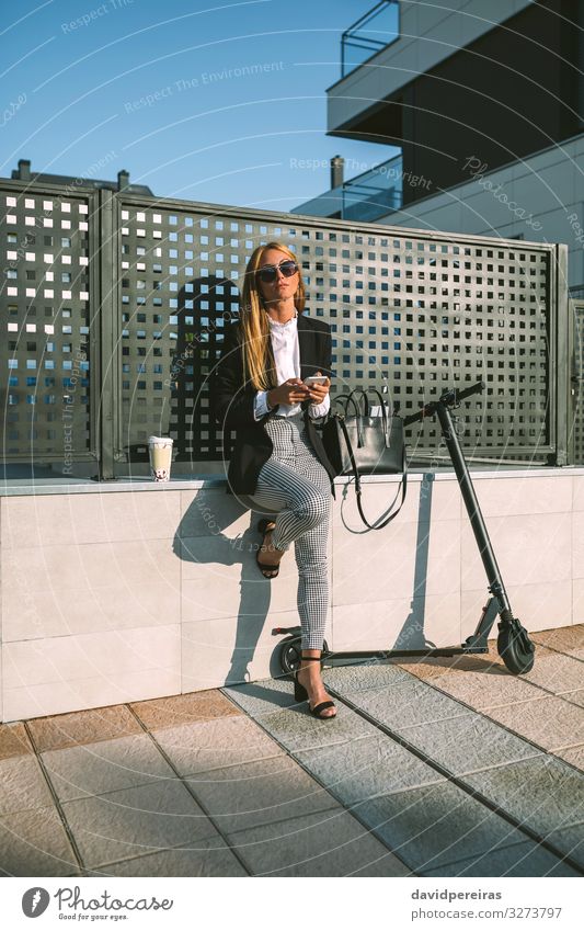 Geschäftsfrau, die ihr Handy mit ihrem Roller benutzt Lifestyle Stil schön PDA Mensch Frau Erwachsene Straße Mode Sonnenbrille sitzen warten modern attraktiv