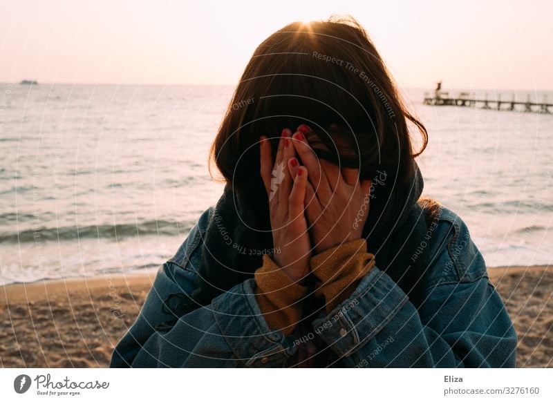 Eine junge Frau steht am Strand und verbirgt das Gesicht in den Händen. Schmerz, Trauer, anonym. feminin Junge Frau Jugendliche Erwachsene 13-18 Jahre