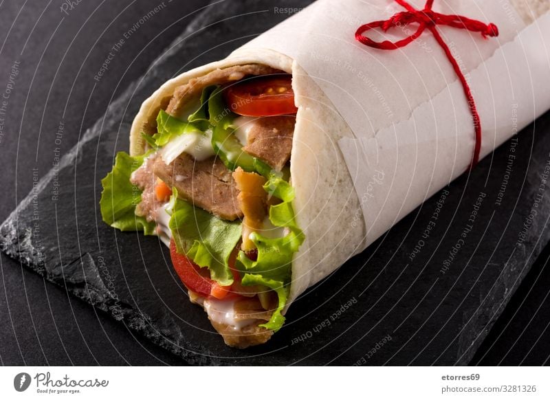 Döner oder Schawarma-Sandwich auf schwarzem Schiefergrund Fleischspieß Kebab Belegtes Brot umhüllen Brötchen Hähnchen Gemüse Tomate Salat Zwiebel