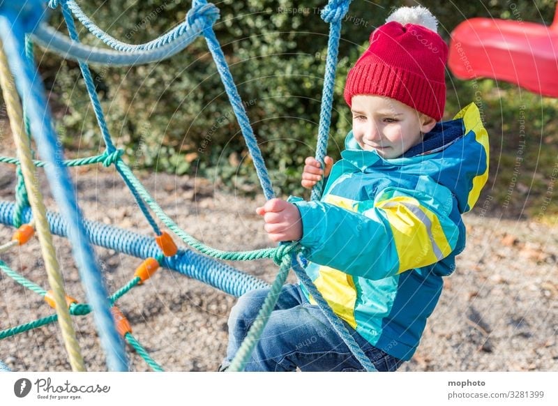Junge auf einem Klettergerüst Kleinkind draußen drei Jahre erlebnis freude jacke junge kindheit klettergerüst klettern lachen lächeln männlich mütze sand