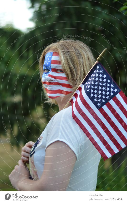 Farbe bekennen | wörtlich genommen | patriotische junge blonde Frau mit amerikanischer Fahne und Flagge aufs Gesicht gemalt im Freien hofft auf den Sieg ihrer Fußballmannschaft