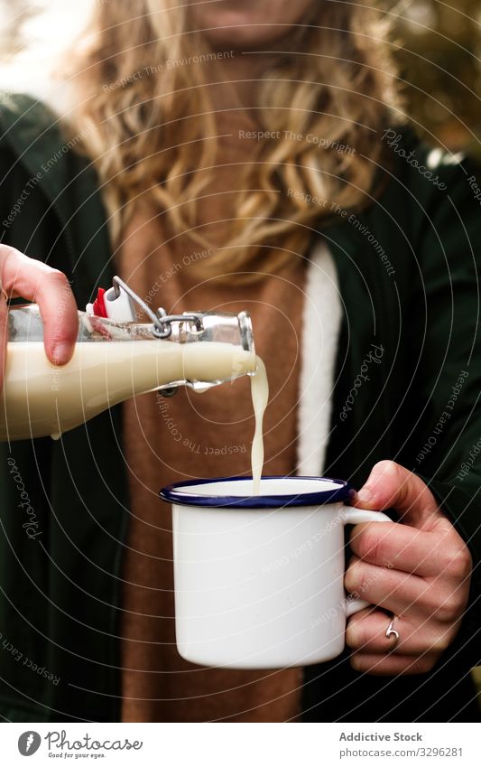 Frau gießt frische Milch aus Flasche in Emaillebecher, während sie sich im Garten erfrischt melken Becher Lebensmittel Hand Getränk Picknick Laktose Molkerei