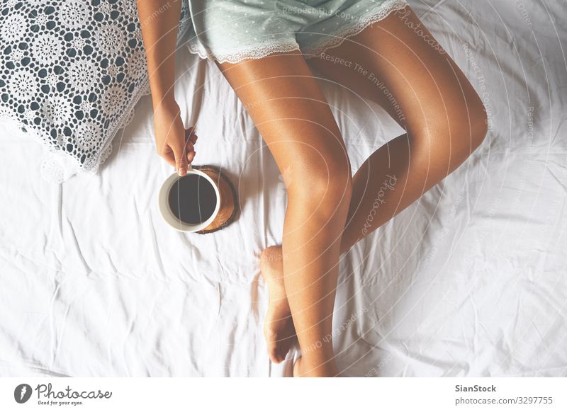 Junge Frau genießt ihren Kaffee im Bett sitzend. Lifestyle Freude schön Leben Erholung Freizeit & Hobby Schlafzimmer Erwachsene Körper Hand Beine 1 Mensch