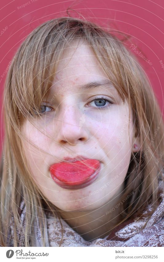 Mädchen, junge Frau Augen, streckt rote Zunge raus. Die Zunge ist rot gefärbt durch Lebensmittel, Farbe, Süßigkeiten, Beeren oder anderer Lebensmittel. Vor einer roten Wand im Hintergrund.