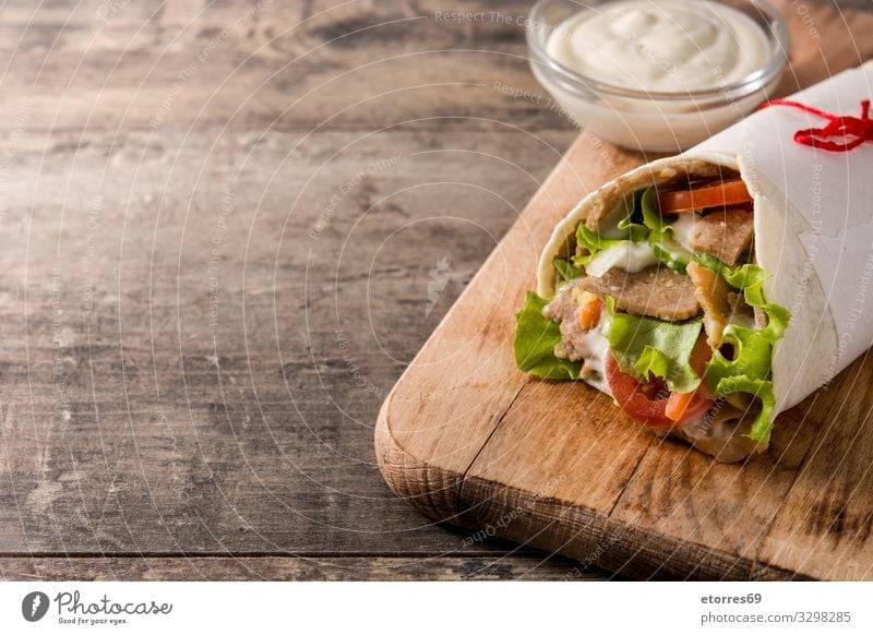 Döner oder Schawarma-Sandwich auf Holztisch. Fleischspieß Kebab Belegtes Brot umhüllen Brötchen Hähnchen Gemüse Tomate Salat Zwiebel Kräuter & Gewürze Saucen