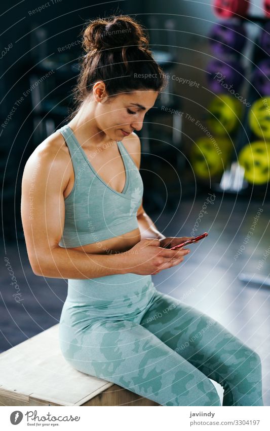 Fitness Frau Beratung ihr Training auf ihrem Smartphone sitzen in einem Sprungkasten im Fitnessstudio Lifestyle Körper Musik Club Disco Sport Telefon PDA