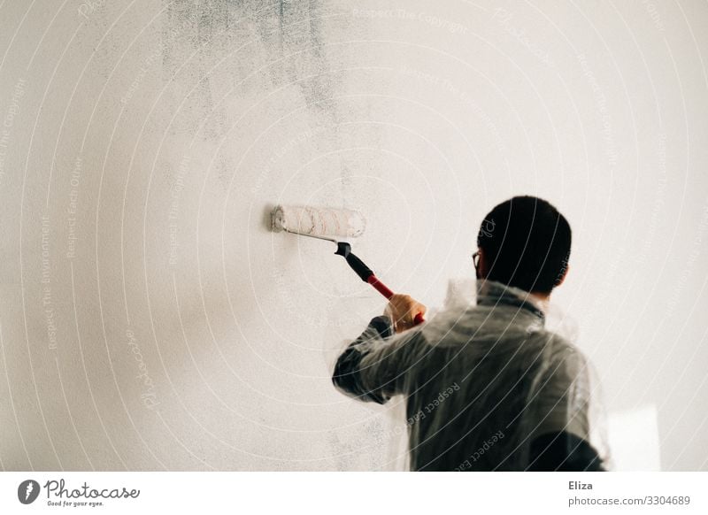 Ein Mann streicht eine Wand mit einer Farbrolle in weißer Farbe Streichen renovieren Maler anstreichen Auszug Anstreicher Anstrich Erwachsene überstreichen
