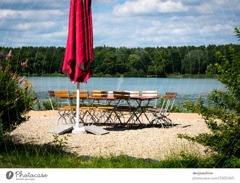 Idylle pur. Ein See , davor ein Sonnenschirm mit einer Gruppe von Stühlen im Kreis. Vorne Grün und im Hintergrund Wald. Freude Erholung Sommer Umwelt