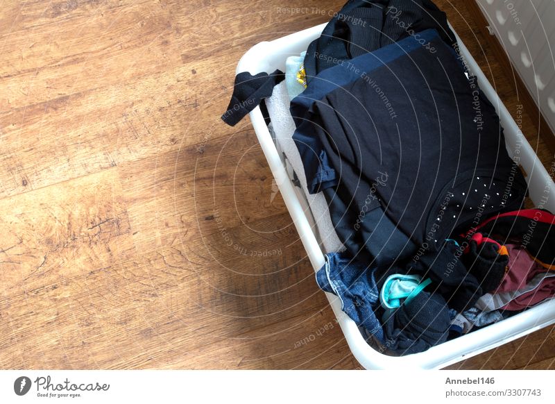 Kleidung in einem vollen Wäschekorb auf einem Laminatboden, Container Mode Bekleidung Hemd Stoff Holz Kunststoff dreckig hell Sauberkeit weiß Farbe Wäscherei