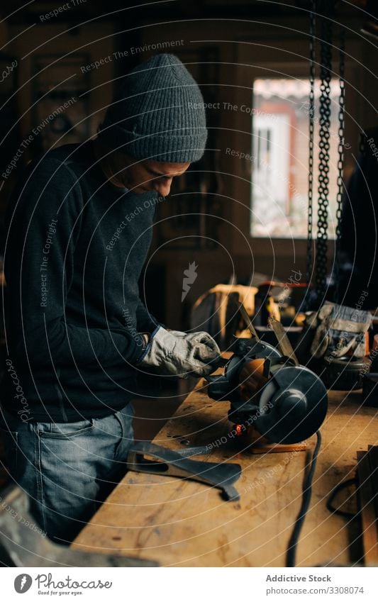 Getreidehandwerker prüft Axt in der Werkstatt Mann Klinge Schleifmaschine prüfen schärfen benutzend Arbeit Werkzeug Handwerk männlich Metallbearbeitung