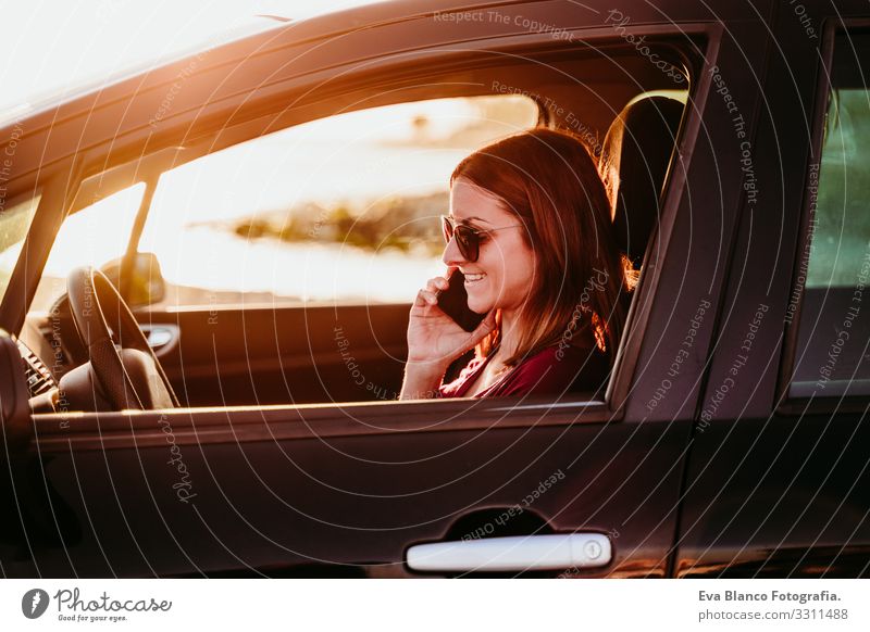 junge Frau, die bei Sonnenuntergang Auto fährt und ein Mobiltelefon benutzt. reisekonzept Jugendliche PKW fahren Strand Fahrer Ferien & Urlaub & Reisen reisend