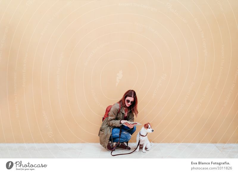 Frau und Hund in der Stadt, gelber Hintergrund. Frau beim Lesen einer Karte. Reise- und Tourismuskonzept reisen Großstadt Landkarte urban Wand jack russell