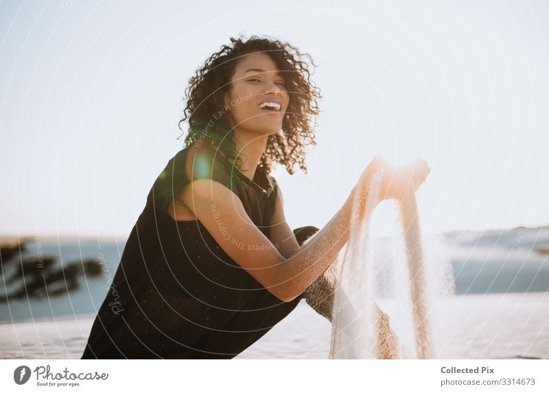 Schöne afrikanische Frau, die lacht und mit dem Sand am Strand spielt Lifestyle Stil schön Wellness Leben Ferien & Urlaub & Reisen Tourismus Ausflug Abenteuer
