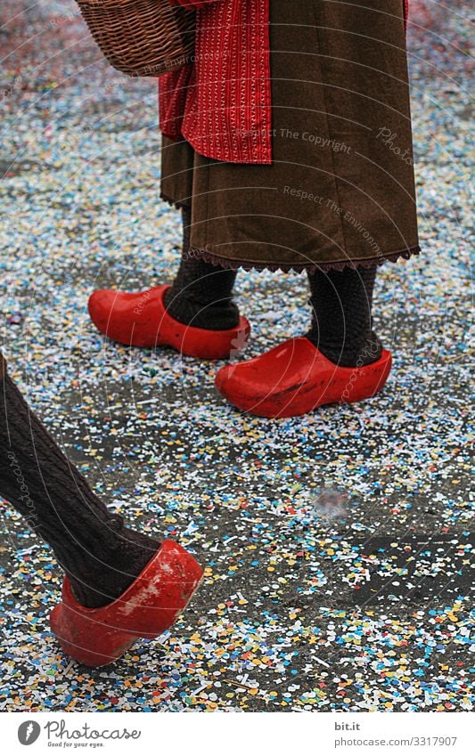 Drei Beine stehen und laufen in roten holländischen Klompen; Holzschuhen und Schürze verkleidet auf der Straße mit Konfetti bedeckt, an Fasching bei einem Karnevalsumzug, der traditionellen Buernfasnachtin Südbaden.