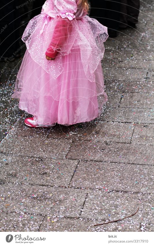 Kleine verspielte, verträumte, hübsche, schöne, süße, verkleidete Prinzessin im rosa, pinken Kleid mit Tüll, steht an Fasching, Karneval als Zuschauer, Besucher am Karnevalszug auf der Straße, auf Konfetti und schaut, beobachtet, genießt das Fest.