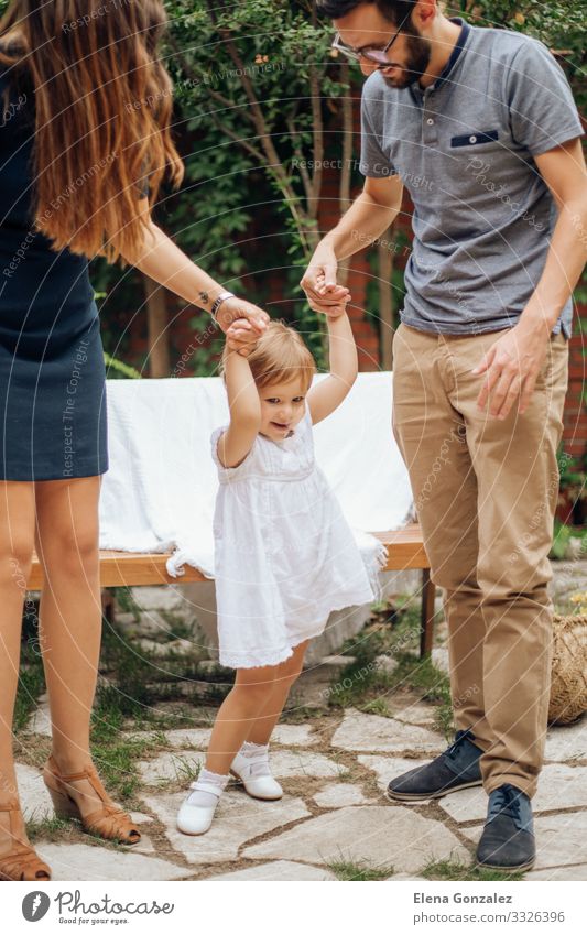 Kleines blondes Mädchen spielt und hält die Hand ihrer jungen Eltern. Spielen Freiheit Garten Hochzeit Kindererziehung Baby Mann Erwachsene Mutter Vater