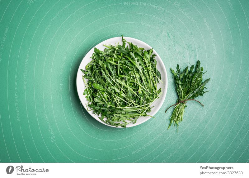 Rucola-Salat und Rucola-Bündel auf grünem Tisch. Frische Kräuter Gemüse Salatbeilage Vegetarische Ernährung Diät Gesunde Ernährung Garten Gartenarbeit Pflanze