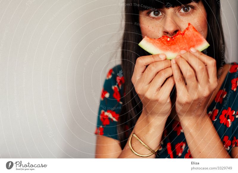 Eine Frau hält sich ein angebissenes Stück Wassermelone vor das Gesicht. Vegane und gesunde Ernährung. Mensch feminin Junge Frau Jugendliche Erwachsene 1