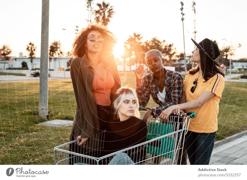 Multirassische Gruppe junger Frauen, die auf der Straße um einen Einkaufswagen herumstehen vielfältig Werkstatt Karre Menschengruppe lässig Herausforderung Witz