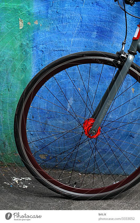 Vorderrad mit Speichen vom Rad, steht geparkt, angelehnt vor blauer, knalliger Wand, bei Pause der Fahhradtour, in der Stadt. Freizeit & Hobby Sport Fitness