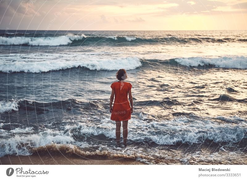Frau in orangem Kleid steht bei Sonnenuntergang im rauen Meer still Lifestyle Erholung Freizeit & Hobby Ferien & Urlaub & Reisen Tourismus Ausflug Abenteuer