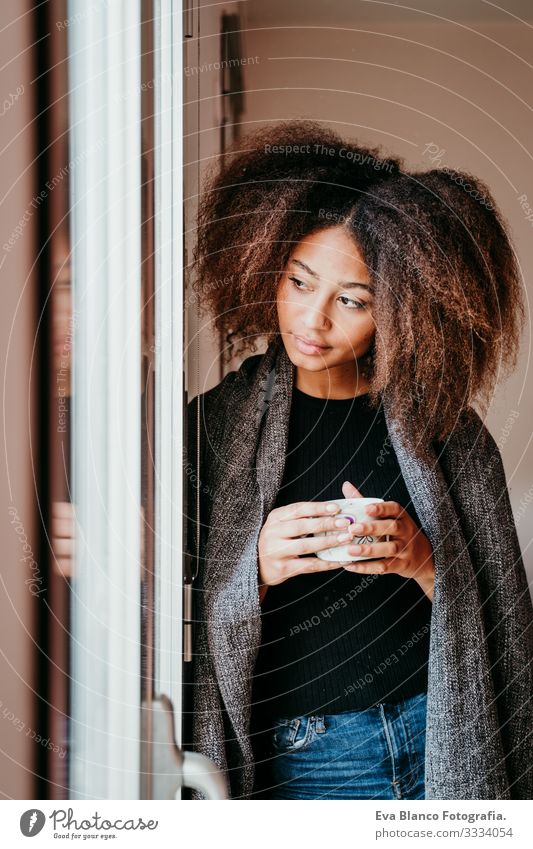 Porträt einer schönen afroamerikanischen jungen Frau am Fenster mit einer Tasse Kaffee. Lebensstil im Haus Afroamerikaner heimwärts urwüchsig