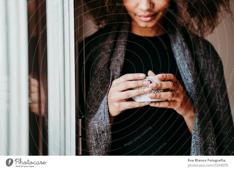 Porträt einer schönen afroamerikanischen jungen Frau am Fenster mit einer Tasse Kaffee in der Hand. Lebensstil im Haus Afroamerikaner heimwärts ethnisch