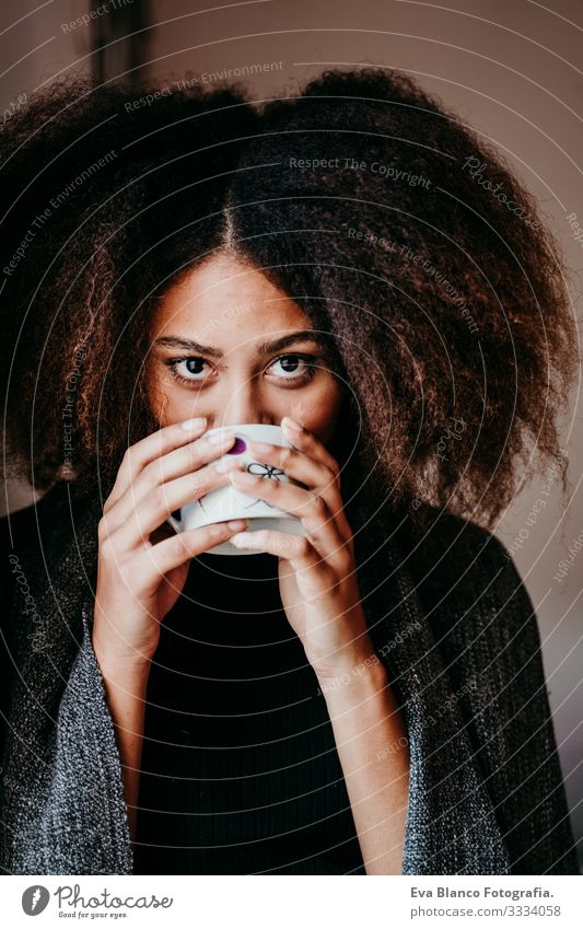 Porträt einer schönen afroamerikanischen jungen Frau am Fenster, die Tee oder Kaffee trinkt. Lebensstil im Haus Afroamerikaner heimwärts ethnisch