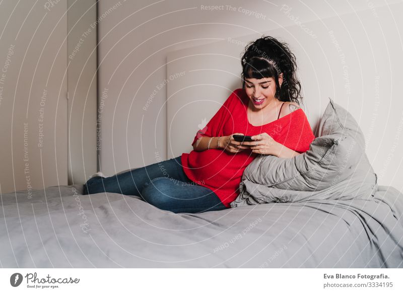 junge schwangere Frau zu Hause, die ein Mobiltelefon benutzt Handy Technik & Technologie benutzend heimwärts Bett PDA erwartend Baby bauchfrei Internet WiFi