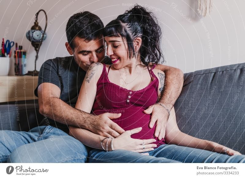 junges Paar zu Hause, das sich umarmt. Glückliche schwangere Frau lächelt Liebe Eltern erwartend heimwärts Sofa Umarmen Küssen Elternschaft Mutterschaft Ehemann